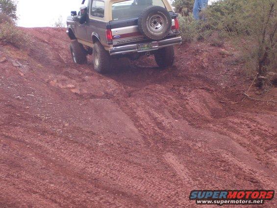 Brown and tan Ford Bronco with spare tire on rear, driving up a dirt hill