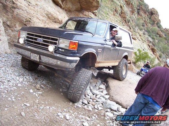 Black Ford Bronco navigating a rocky trail with a person driving and another person on an ATV behind it