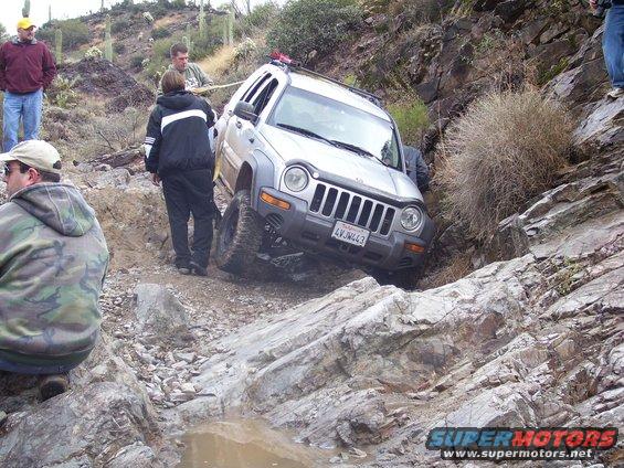 Silver Jeep Liberty navigating a steep, rocky off-road trail with people watching