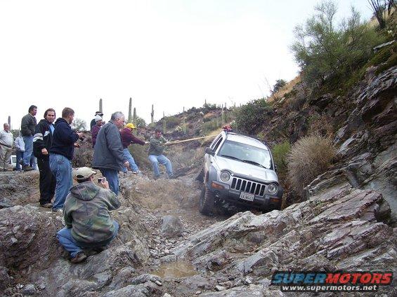 People pulling a Jeep Liberty out of a ditch on a rocky trail