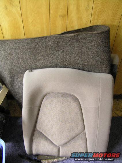 Car seat and rolled up carpet in front of wood-paneled wall. Supermotors.net logo visible