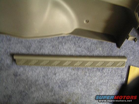 Gray plastic interior trim piece with diagonal textured lines on a blue fabric surface