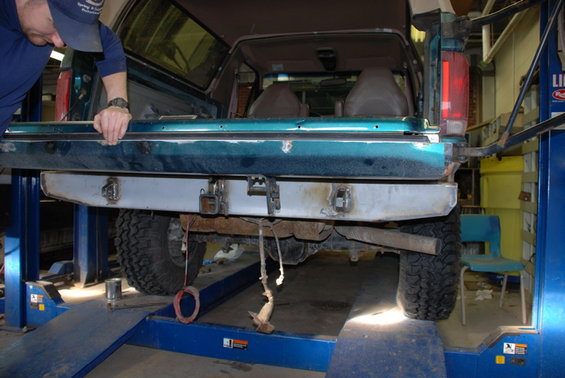 Green Ford Bronco with custom metal rear bumper, lifted on a blue car lift