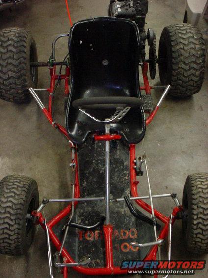 Go-kart with red frame, black seat, and four knobby tires. Text on the floor pan reads "TORNADO 100"