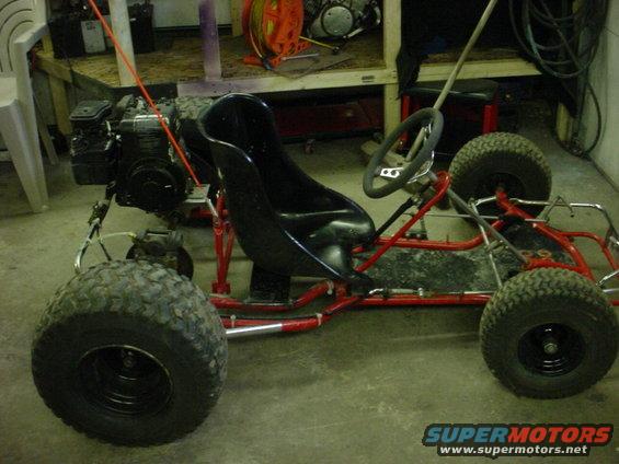 Go-kart with red frame, black seat, and large tires. Engine is visible