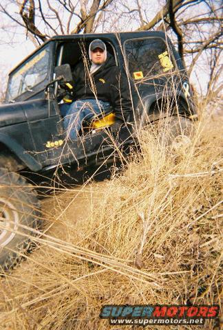 Black 1981 Jeep CJ7 with yellow seat and driver, angled from the front-left in dry grass