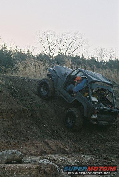 Black Jeep CJ climbing a dirt hill, driver wearing orange hat