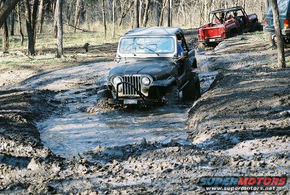 1981 Jeep CJ7 and other Jeeps navigating a muddy trail in a wooded area