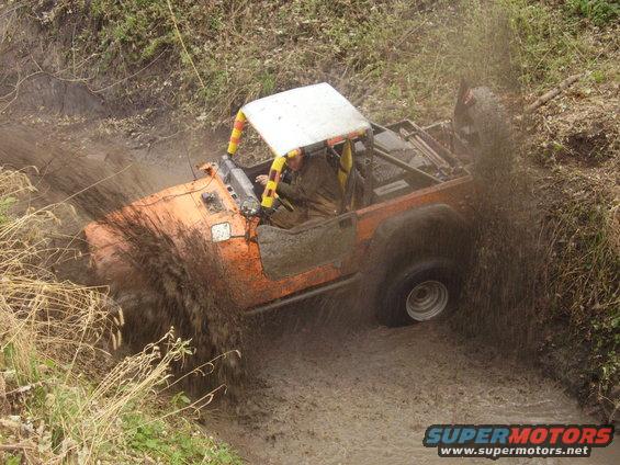 1981 Jeep CJ7 driving through a muddy ditch, kicking up water and dirt