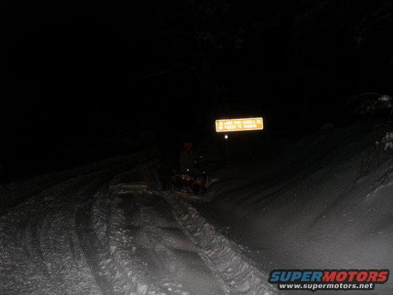 ATV on snowy trail at night with a yellow sign