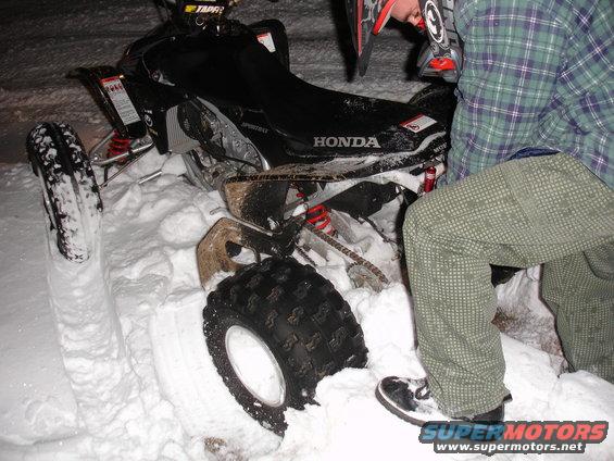 Black 2005 Honda TRX 450 R ATV partially buried in snow, with a person in a plaid shirt and patterned pants standing nearby