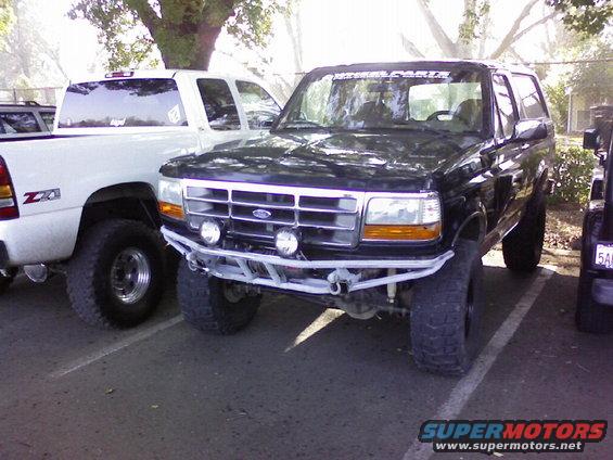 1995 Ford Bronco front end with aftermarket bumper and lights, parked next to a white pickup truck