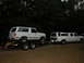 1986 Ford F-350 - A white Ford Bronco is loaded onto a trailer, while a white Ford F-350 crew cab dually with a camper shell is parked nearby.