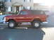 1979 Ford Bronco - Side view of a lifted red 1978 Ford Bronco parked in front of a house with a silver van in the background.
