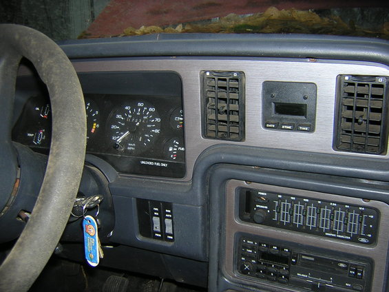 Dashboard of a 1987 Ford Thunderbird with a dusty steering wheel, instrument cluster, and radio