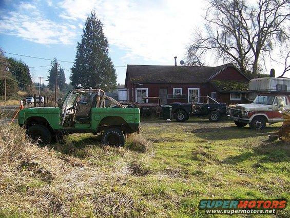 Green SUV with roll cage, missing doors and top, parked in dry grass