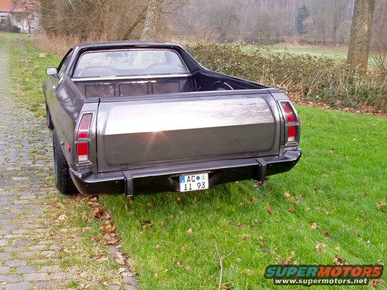 Dark gray 1972 Ford Ranchero rear quarter view, parked on grass next to a cobblestone path