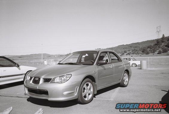 Silver sedan parked on asphalt, front 3/4 view. Another white car is to the left