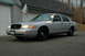 2003 Ford Crown Victoria - Silver 2003 Ford Crown Victoria police car with a spotlight on the driver's side is parked in front of a garage.