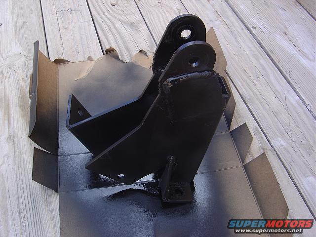 Black painted metal bracket sitting in a cardboard box on a wooden surface