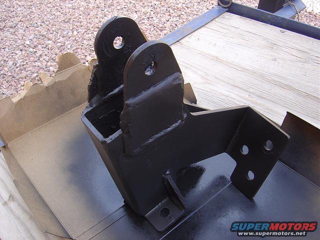 black metal bracket with holes, sitting on a trailer bed and in a cardboard box