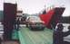 1989 Ford Bronco - A brown Ford Bronco is being driven onto a ferry, with a large red structure and another vessel in the background.