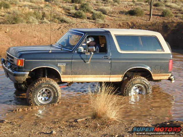 1991 Ford Bronco driving through muddy water, side view