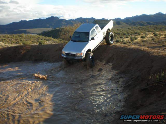 Silver pickup truck driving through muddy water on an incline