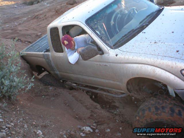 Silver pickup truck stuck in mud, driver looking down