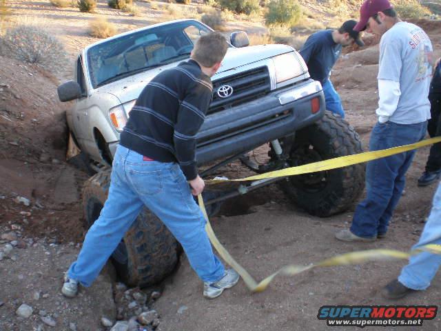 Truck stuck in a ditch, people trying to pull it out with a yellow strap
