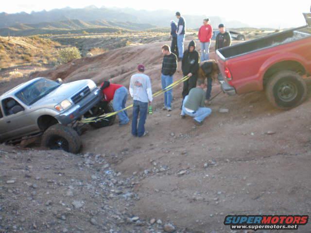 Silver pickup truck stuck in dirt, being pulled by a red truck