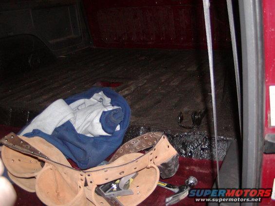 Interior of a truck bed with tools and a rolled-up blanket