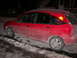 2002 Ford Focus - A red Ford Focus hatchback is parked on a street covered in snow and slush at night.