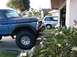 1978 Ford Bronco - A blue pickup truck is parked in front of a garage, with a white minivan visible in the background.