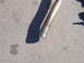 1996 Ford Probe - A section of an exhaust pipe lies on a concrete surface, casting a long shadow.