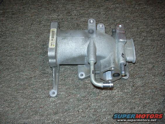 Aluminum intake manifold with a label reading YWTE-AA, resting on a carpeted surface