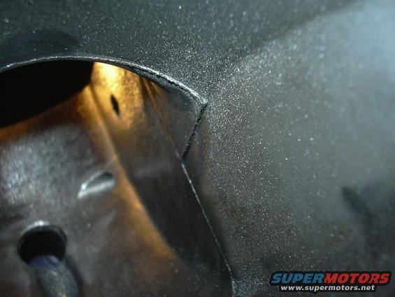 Close-up of a dark, textured vehicle body panel with a light source visible in an opening