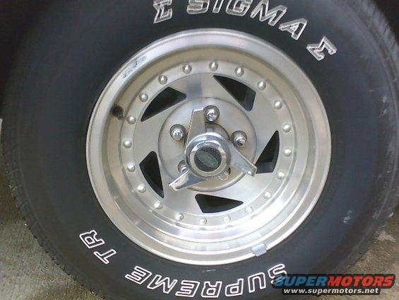 Close-up of a chrome wheel with a three-pronged spinner and a black tire with white lettering reading "SUPREME TR" and "SIGMA"