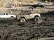 1978 Ford Bronco - A heavily mud-covered 1978 Ford Bronco navigates a muddy terrain, with other vehicles and spectators in the background.