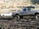1978 Ford Bronco - A silver pickup truck navigates through a muddy terrain, with another white truck visible in the background.