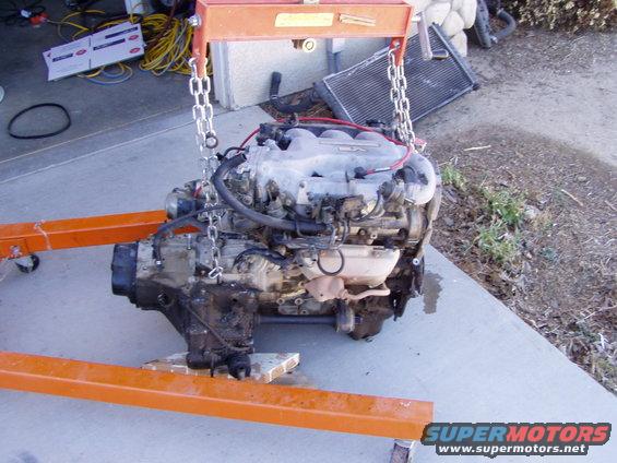 Engine assembly suspended by chains from an orange engine hoist