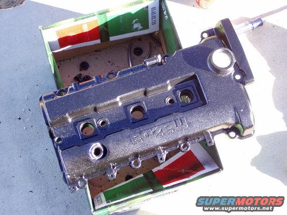 Silver engine valve cover with 'MAZDA' visible, resting in a box