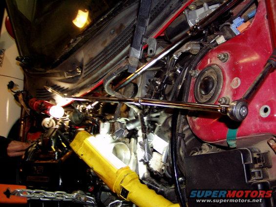 Mechanic working on car engine with tools and yellow flashlight