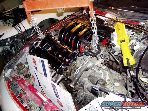 Engine components and chains suspended by an engine hoist over a car engine bay