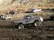 1978 Ford Bronco - A blue 1978 Ford Bronco navigates a muddy off-road course with other vehicles and spectators in the background.