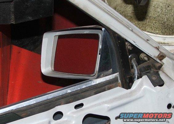 Close-up of a car's side mirror assembly, showing the mirror housing and mounting hardware