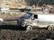 1978 Ford Bronco - A black van is stuck in deep mud, with other vehicles and spectators in the background.