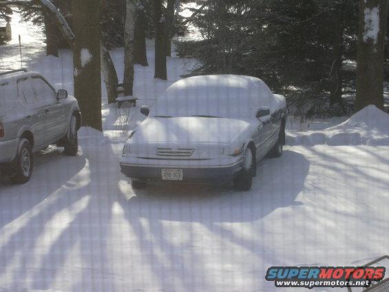 1996 Ford Crown Victoria covered in snow, parked next to an SUV