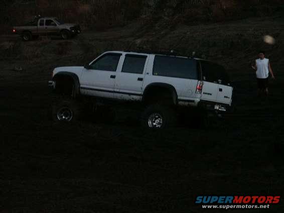White SUV with lifted suspension and roof rack parked on a dirt hill