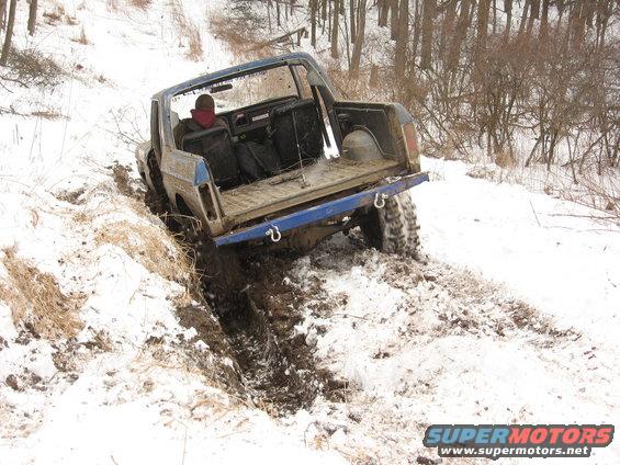 blue off-road vehicle stuck in mud and snow on a wooded trail
